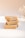 Three stacked bars of handmade soap with a natural, beige color sit on a soft white surface. A delicate sprig of dried flowers is visible in the background, adding an elegant touch to the minimalistic composition.
