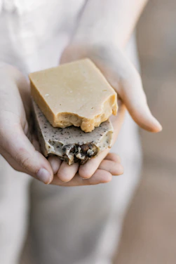 Close-up of a hand holding a creamy, earthy-toned organic soap bar with natural textures.