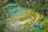 A vibrant landscape featuring a series of turquoise pools connected by small waterfalls, surrounded by lush greenery and dense forest. The scene is an overhead view showcasing the natural pattern and flow of water and vegetation.
