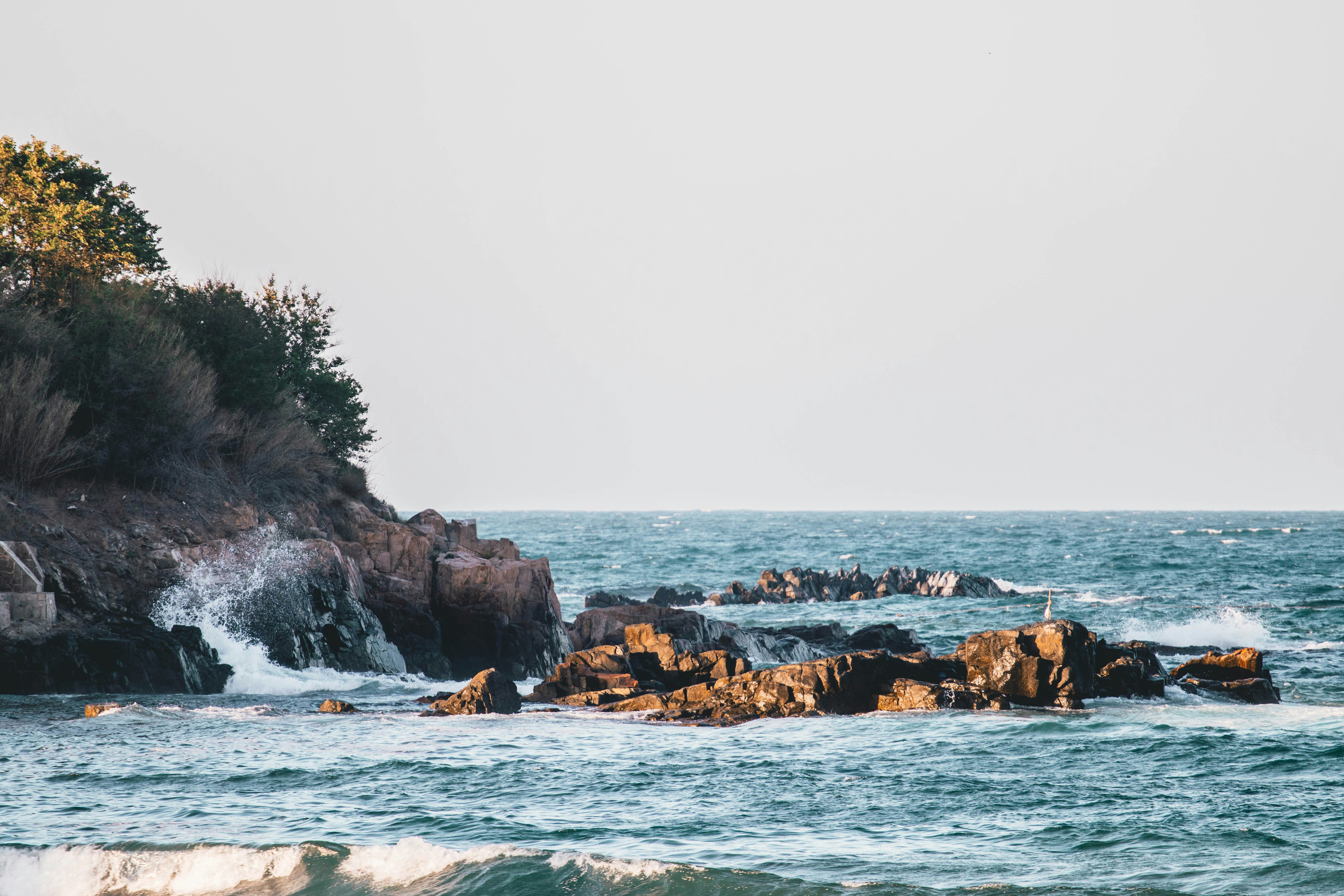 brown rocky shore with ocean waves crashing on shore during daytime