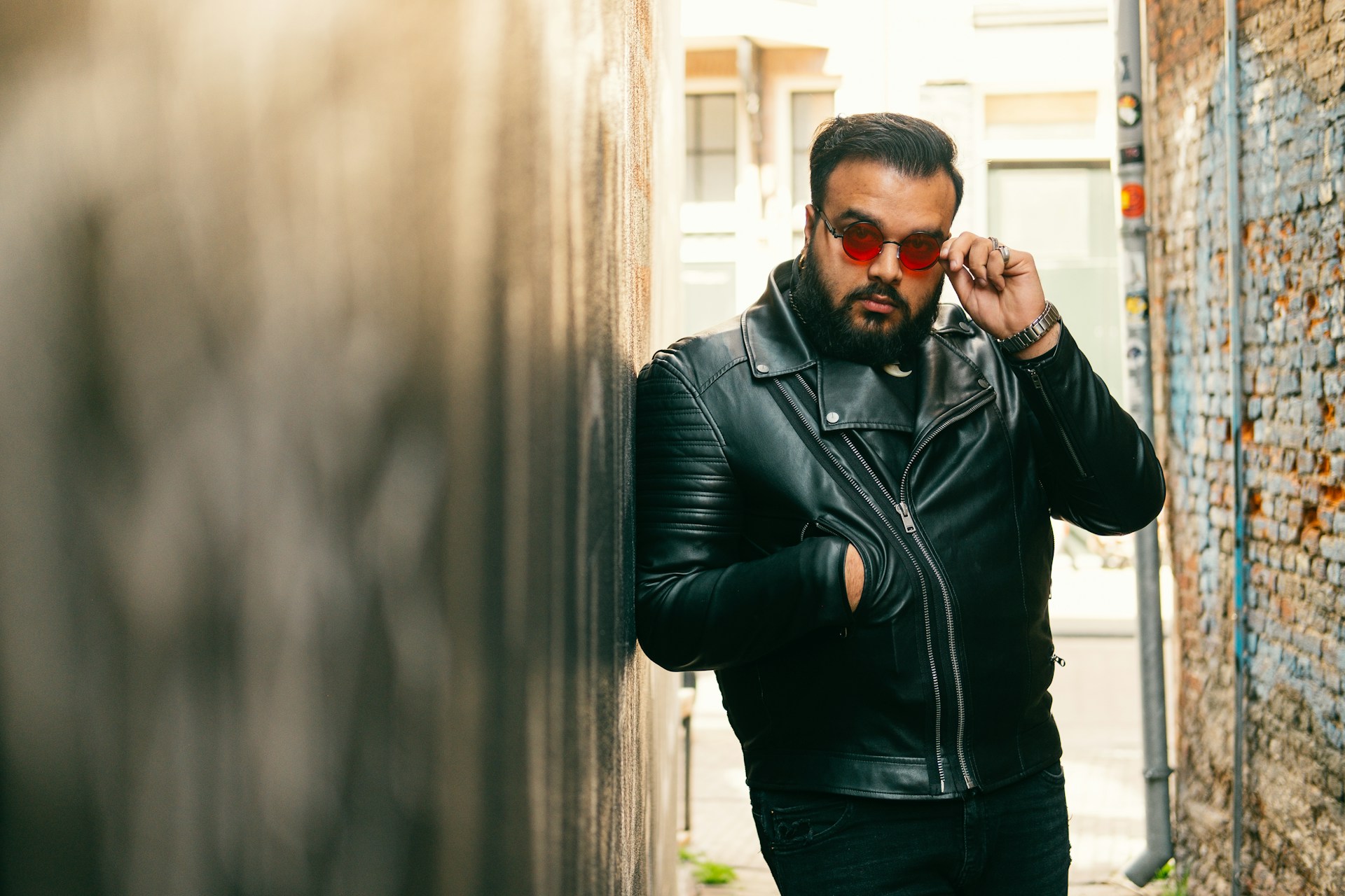 man in black leather jacket and black sunglasses standing beside brown wall