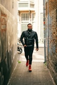 man in black leather jacket and black pants standing beside gray concrete wall during daytime