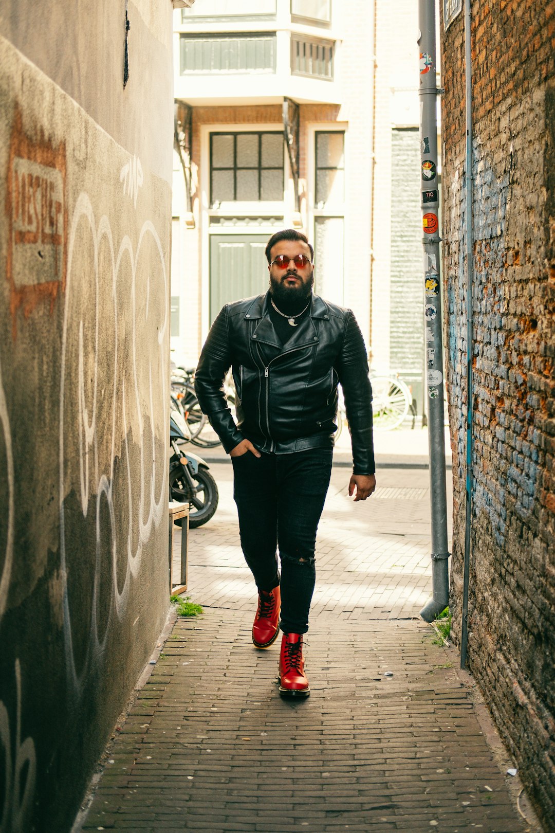 man in black leather jacket and black pants standing beside gray concrete wall during daytime