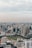 An urban cityscape featuring a densely packed skyline of modern high-rise buildings. The architecture includes a mixture of commercial skyscrapers and residential buildings. In the foreground, a large green park provides contrast to the urban setting, and the cloudy sky suggests a calm atmosphere.