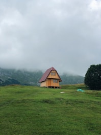 brown wooden house on green grass field near green mountains under white clouds during daytime