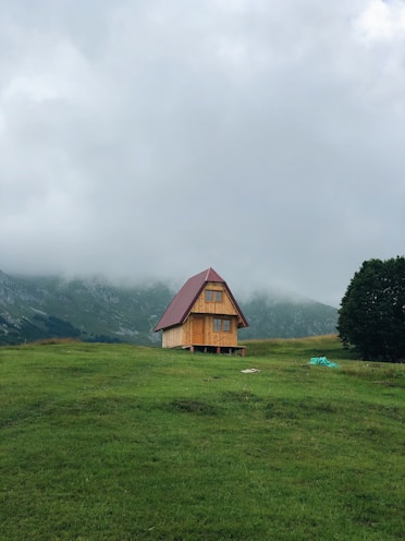 brown wooden house on green grass field near green mountains under white clouds during daytime