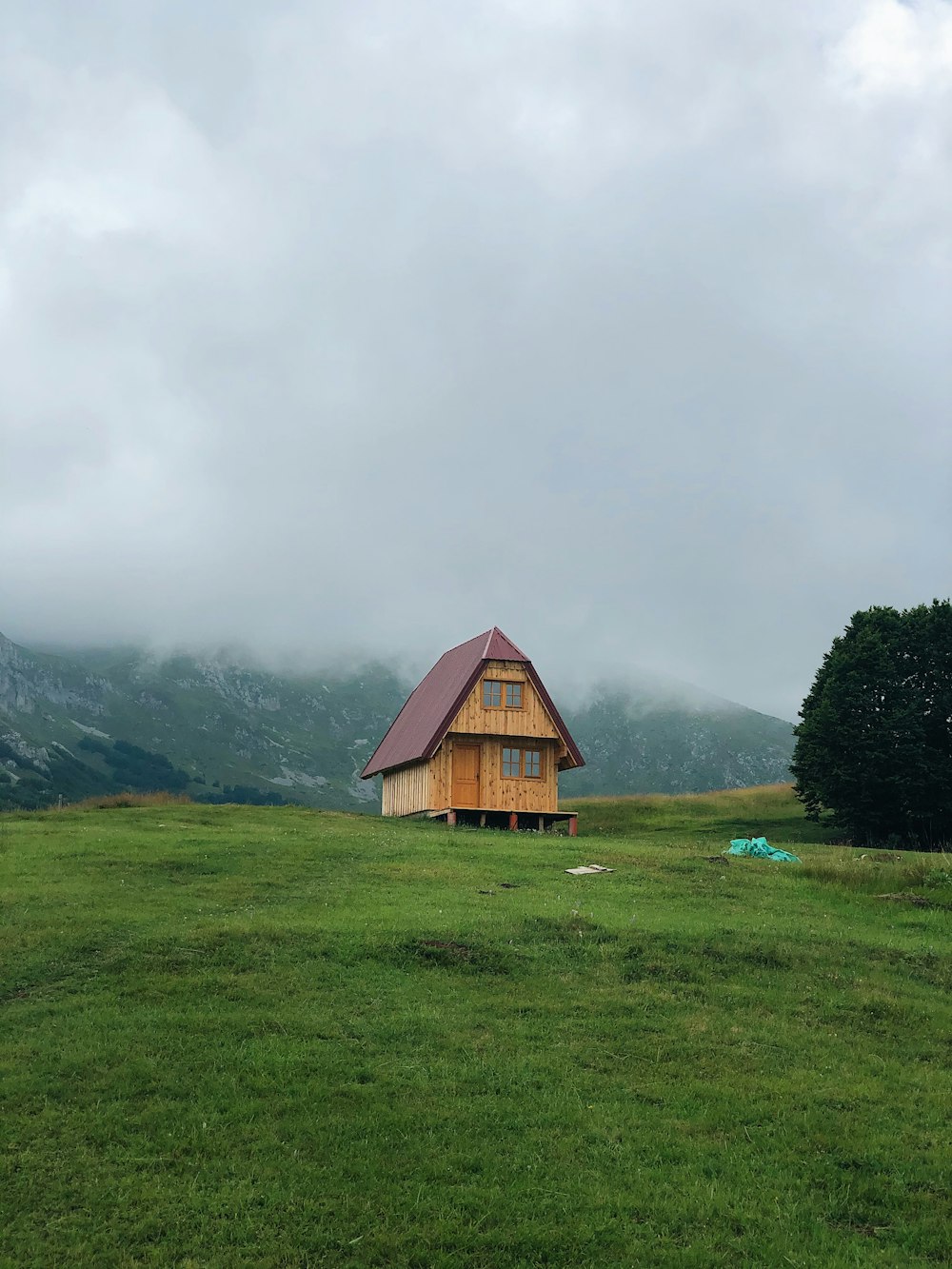 Braunes Holzhaus auf grünem Grasfeld in der Nähe von Green Mountains unter weißen Wolken tagsüber