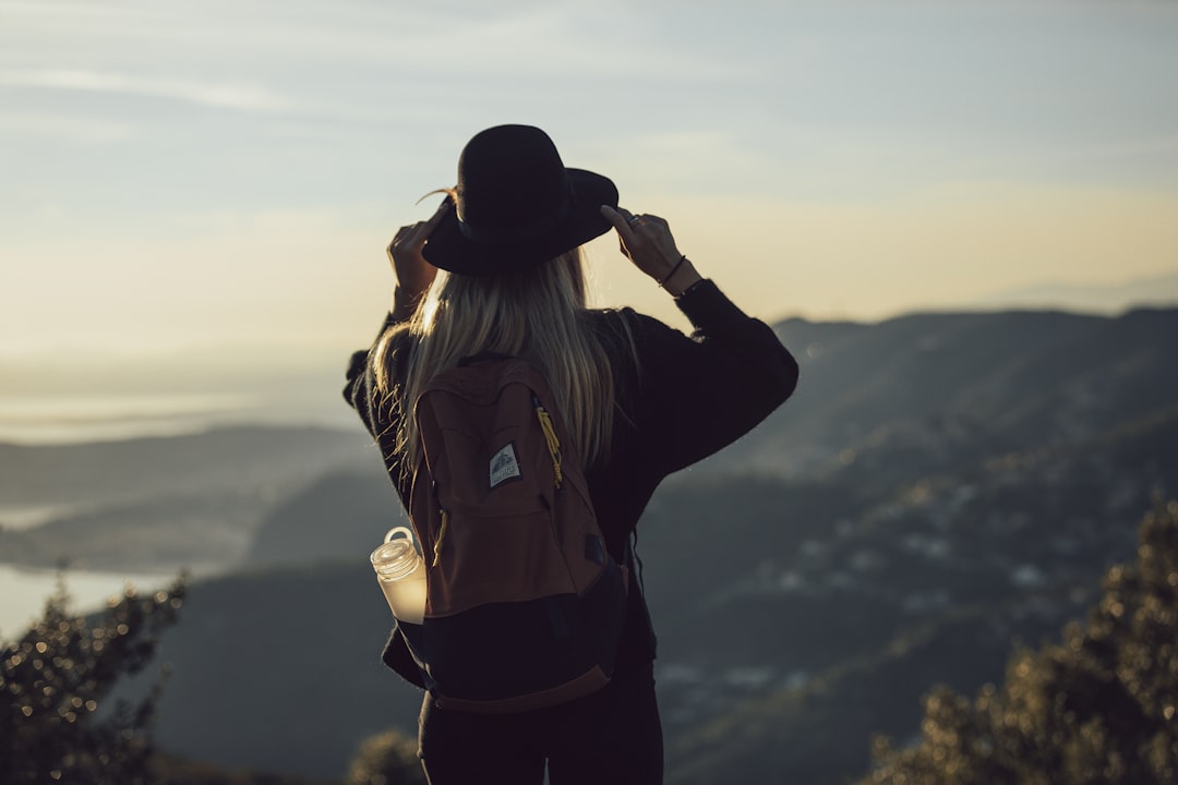 woman in gray hoodie and black pants wearing black hat standing on top of mountain during, Always ready for an adventure