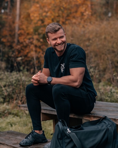 man in black long sleeve shirt and black pants sitting on brown wooden bench during daytime