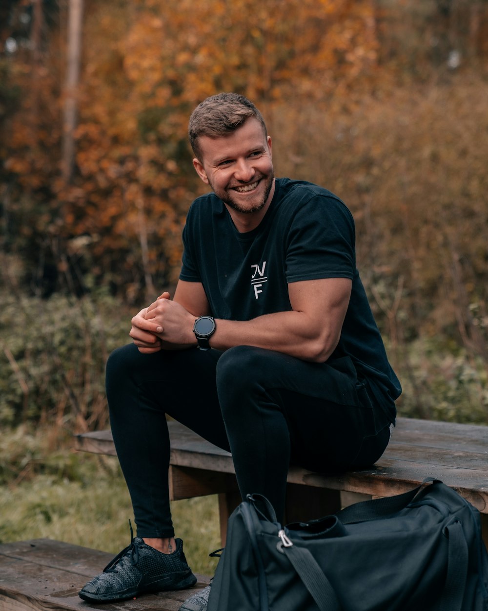 man in black long sleeve shirt and black pants sitting on brown wooden bench during daytime