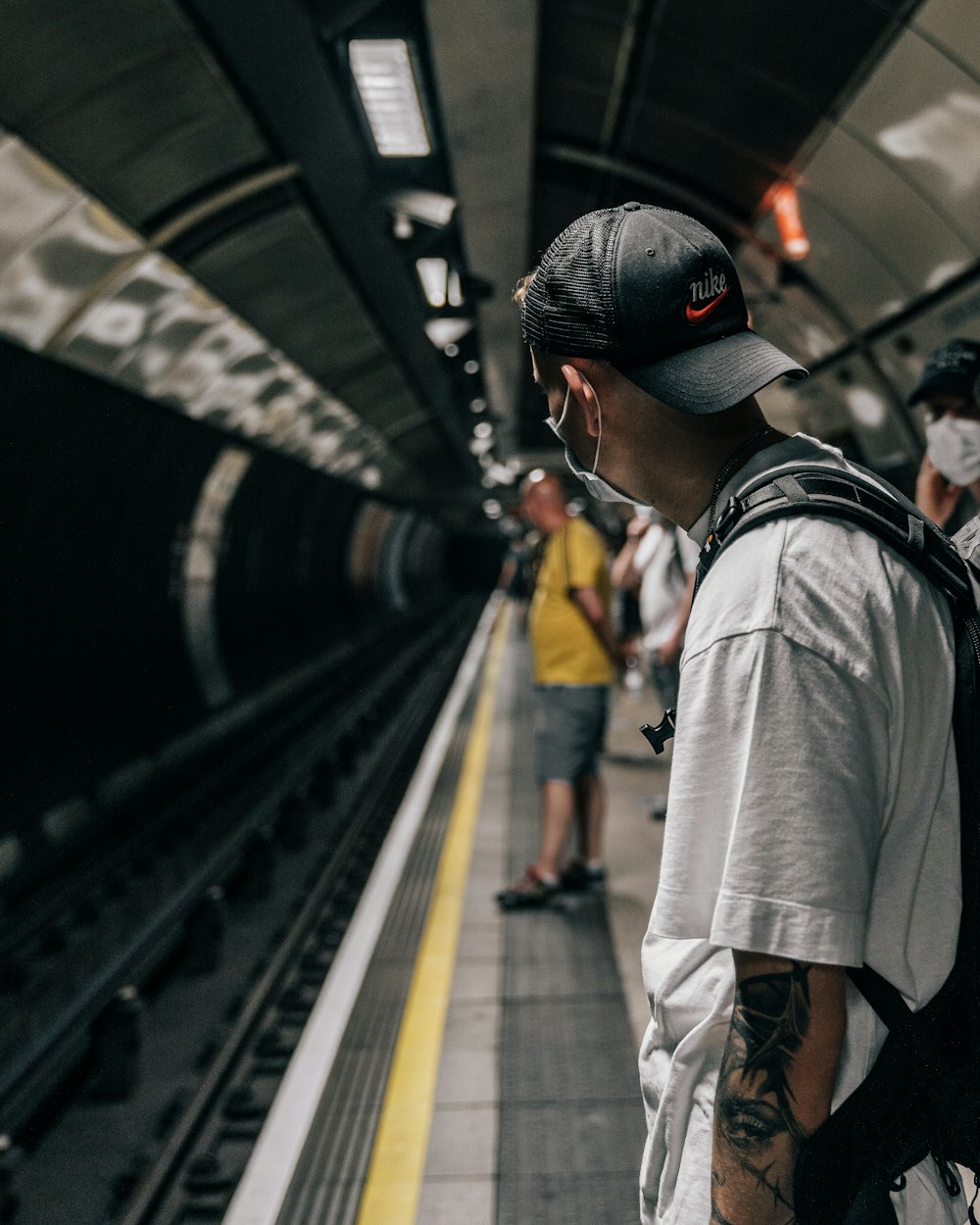 man in grey shirt and black cap standing on train station