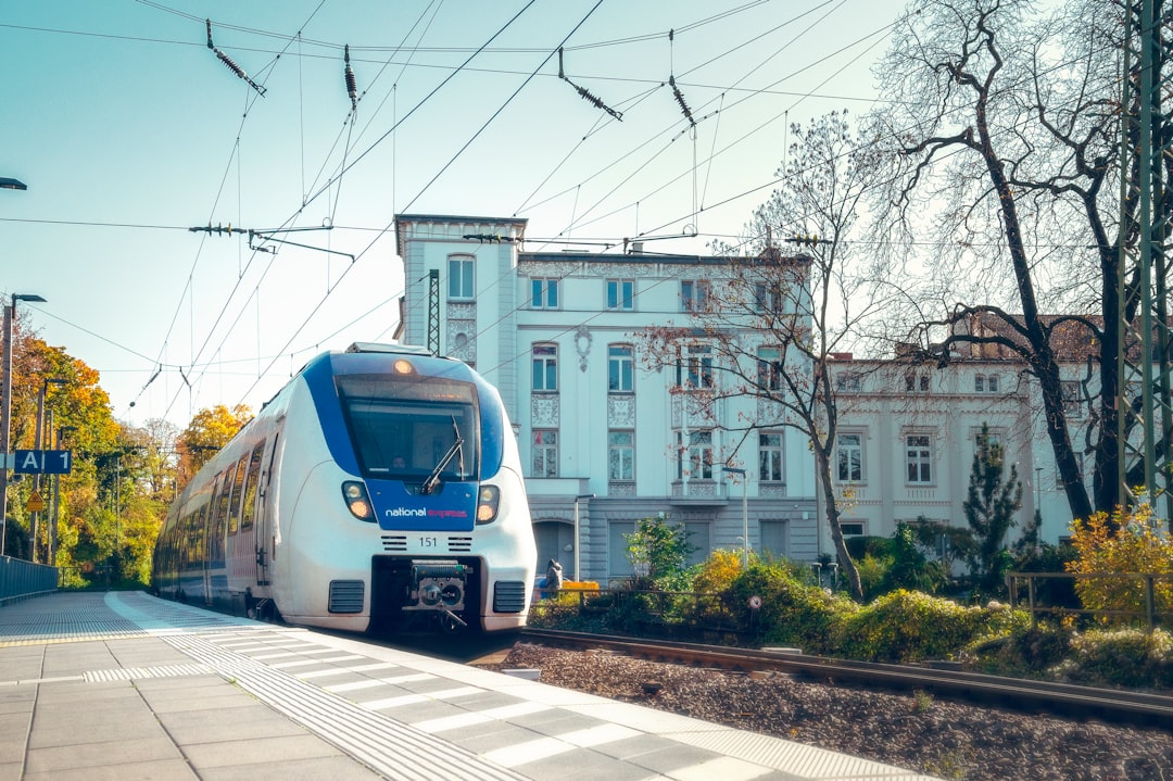 blue and white train on rail road near white concrete building during daytime