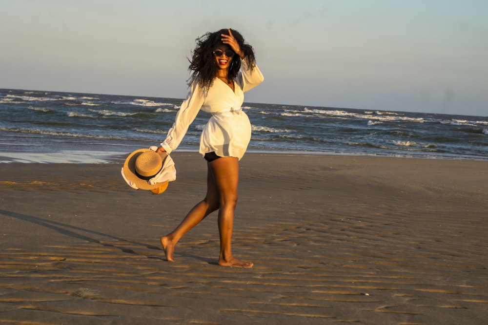 낮 동안 해변에 서 있는 갈색 모자를 들고 있는 흰색 드레스를 입은 여자