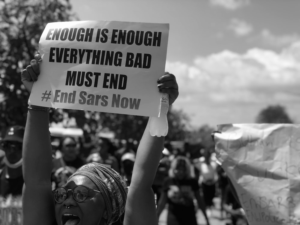 a woman holding a sign that says enough is enough everything bad must end