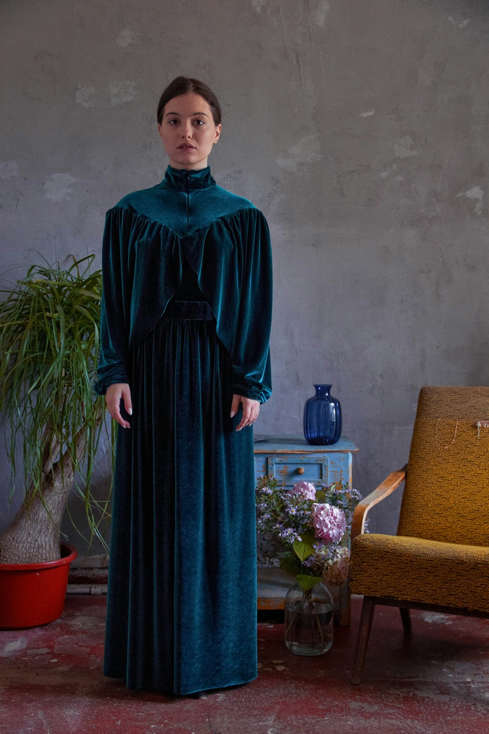 woman in blue long sleeve dress standing beside brown couch