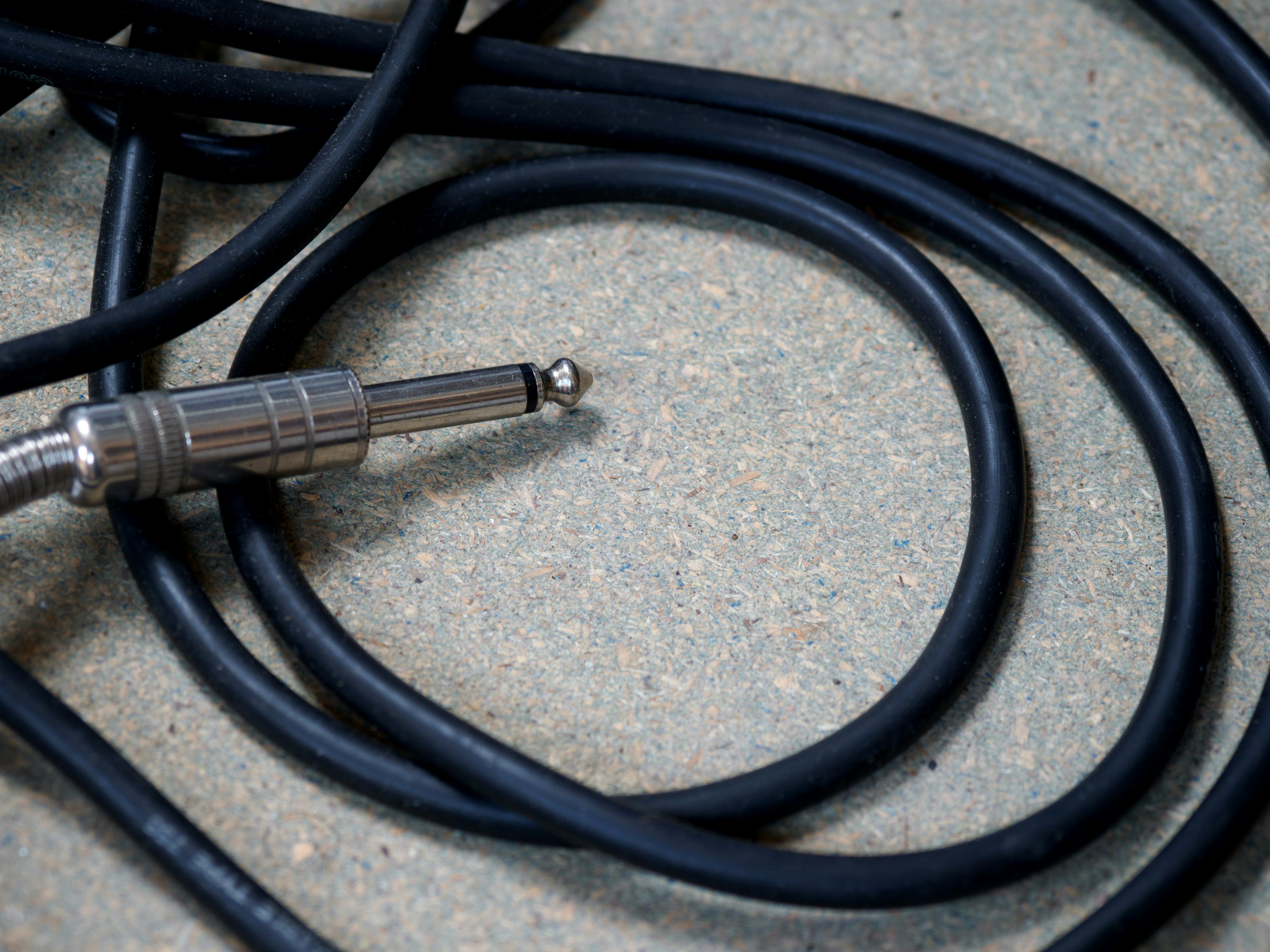 Zbliżenie na stary, postrzępiony lub uszkodzony kabel gitarowy leżący na podłodze obok sprzętu, symbolizujący potencjalne źródło szumów i zakłóceń.