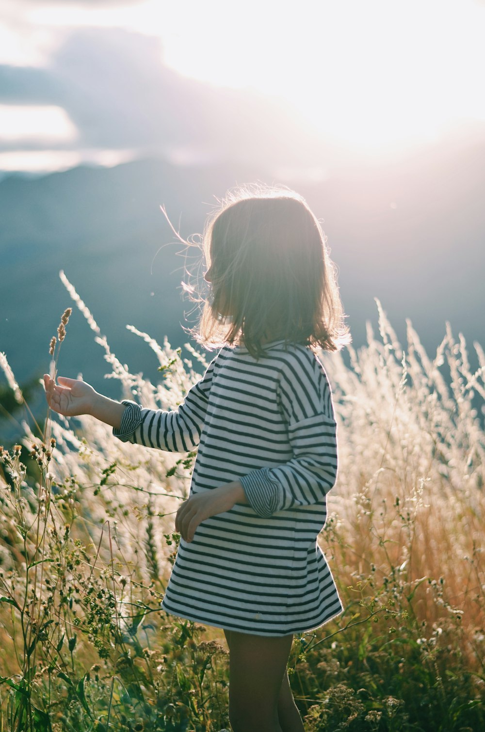 fille en chemise à manches longues rayée noire et blanche debout sur le champ d’herbe verte pendant la journée