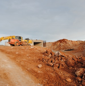 yellow excavator near brown rock formation during daytime