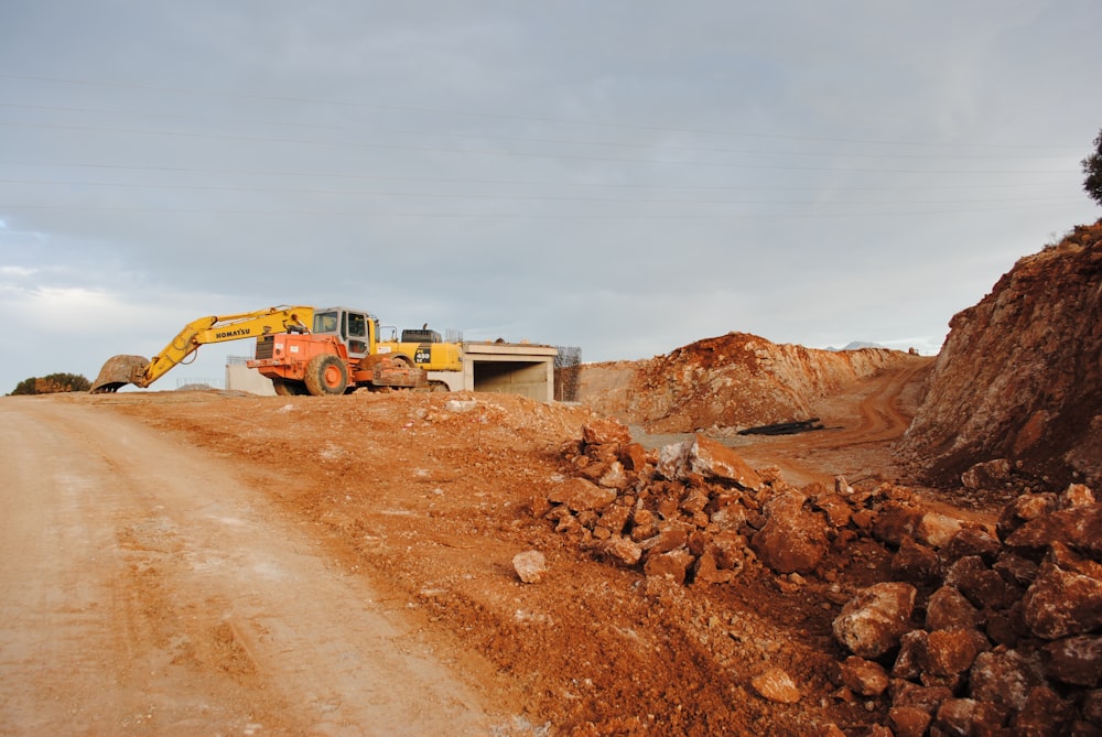 yellow excavator near brown rock formation during daytime