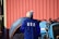 A person wearing a blue jacket with 'USA' printed on the back is standing in front of a tractor. The background includes a corrugated red metal wall and a large tire.