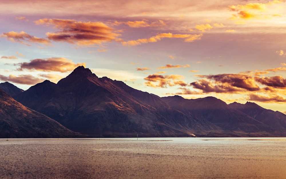 brown mountain near body of water during sunset