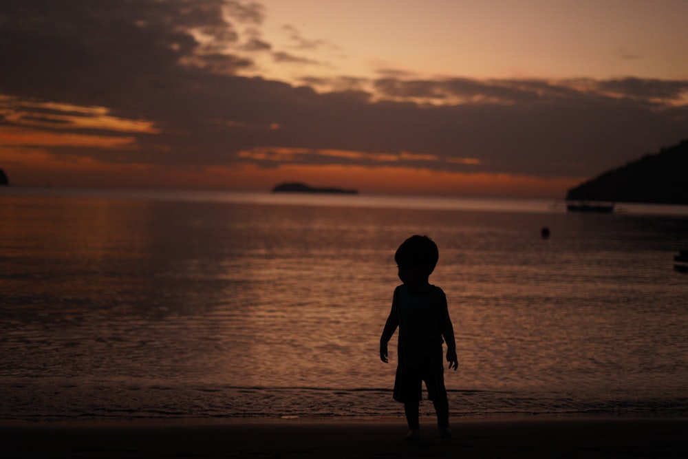 silhouette of child standing on beach during sunset