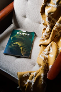 A comfortable armchair with a knitted blanket draped over it, next to a small stack of magazines.