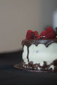 An elegant raspberry Belgian chocolate cake adorned with fresh raspberries and subtle chocolate curls on a soft beige background.