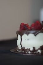 A delectable cake adorned with a rich chocolate glaze cascading down its sides. Fresh raspberries are arranged artfully on top, adding a vibrant touch of color. The focus on the cake creates a mouthwatering and inviting appearance.