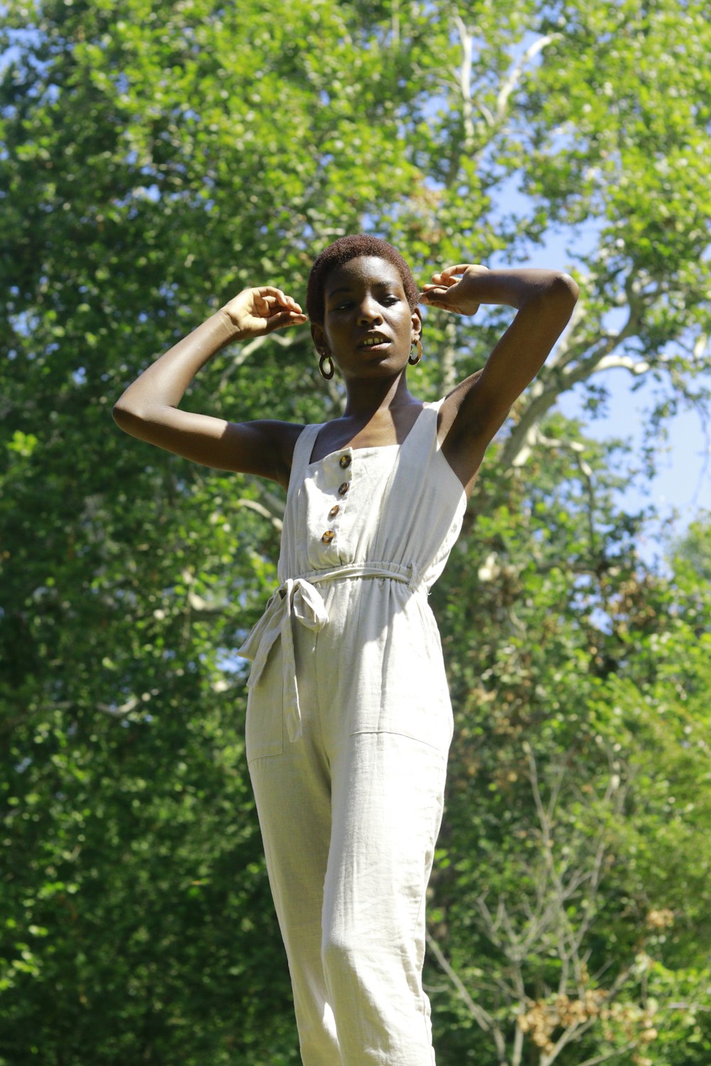 woman in white sleeveless dress standing and raising her hands