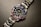 A luxury wristwatch with a metallic strap and a black dial. The bezel is adorned with alternating blue and pink gemstones, and the dial features white hour markers and a date window.