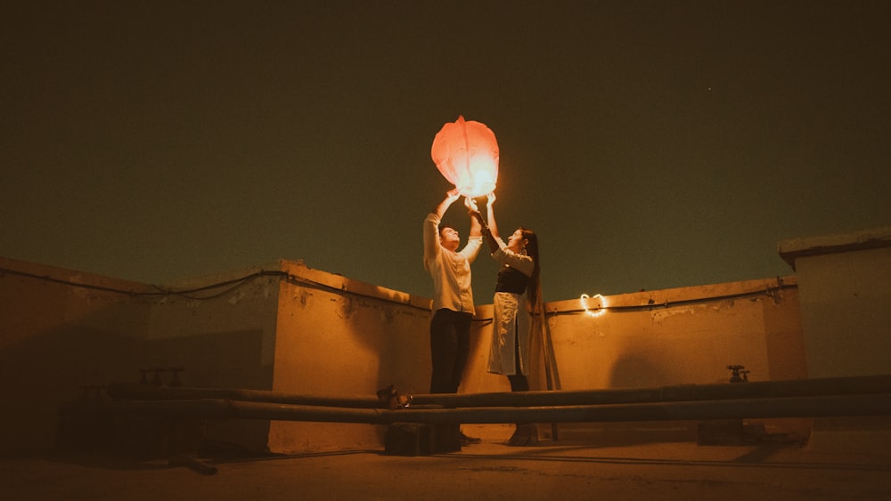 silhouette of 2 person holding balloons during sunset