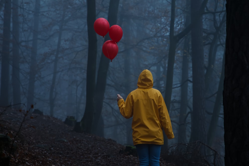 child in yellow hoodie standing on forest during daytime