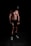 A muscular person stands shirtless in a dark environment, holding dumbbells with a focused posture. The individual wears a cap with a distinctive logo, shorts, and sneakers, suggesting a fitness or workout setting.