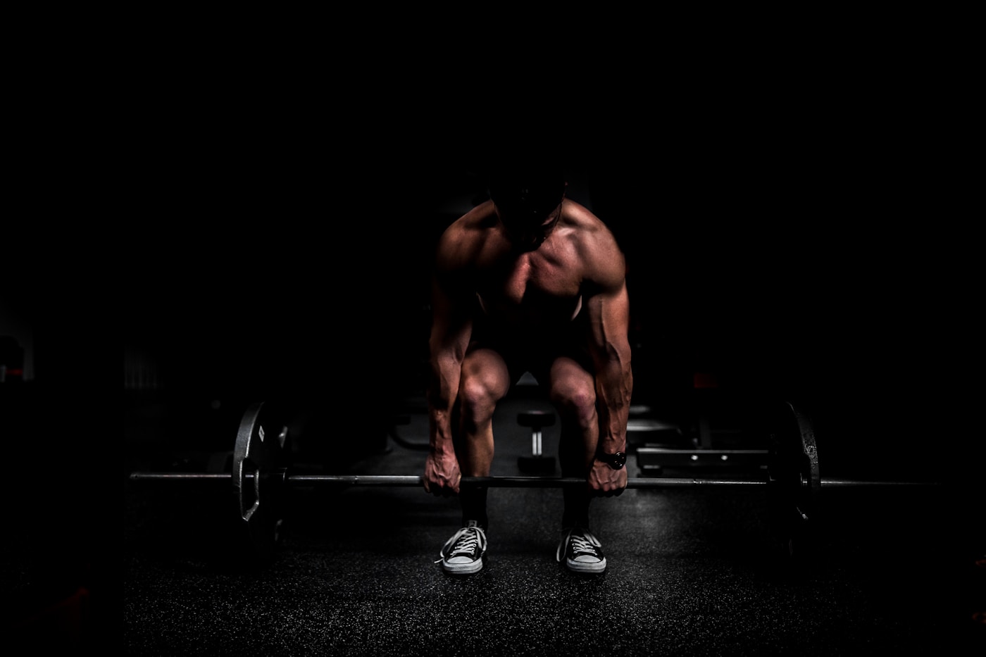 A lifter setting up under a loaded barbell in a dark gym