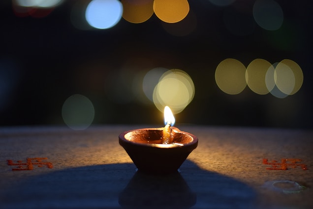 A warm-lit close-up of a traditional diya lamp glowing softly against a backdrop of carved stone temple walls.