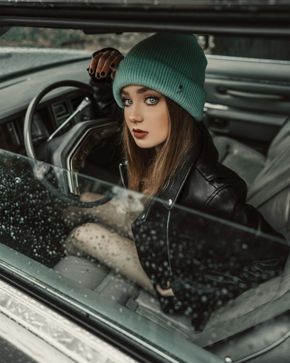 woman in black leather jacket and green knit cap sitting on car