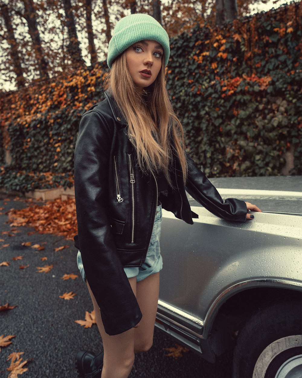 woman in black leather jacket and blue denim shorts sitting on black car