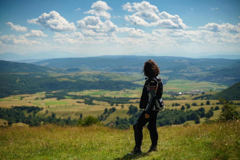 Femme en veste noire debout sur le champ d’herbe verte pendant la journée