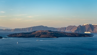A scenic view of a cruise ship sailing near a tropical island under a clear sky.
