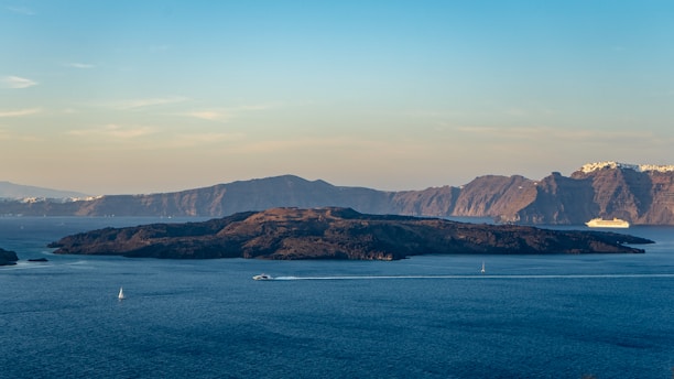 A scenic view of a cruise ship sailing near a tropical island under a clear sky.