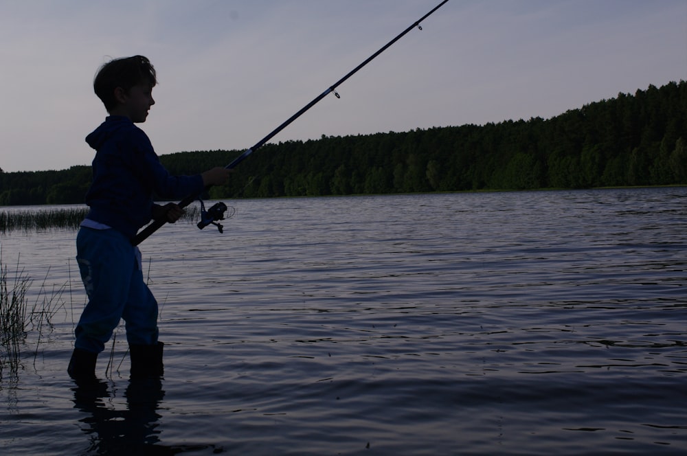 boy in black jacket fishing on lake during daytime