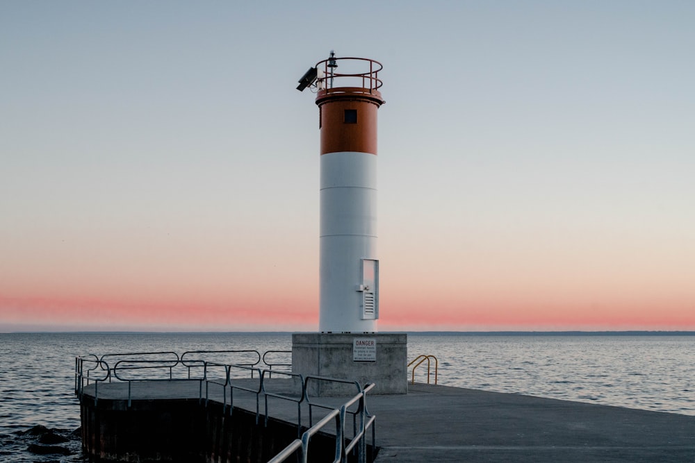 昼間の海近くの白と赤の灯台