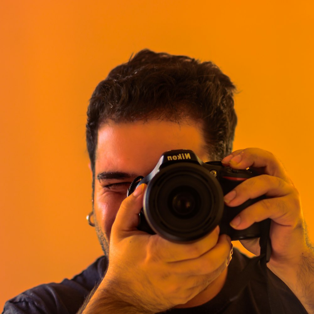 Uomo in camicia nera a maniche lunghe che tiene la fotocamera reflex digitale Nikon nera