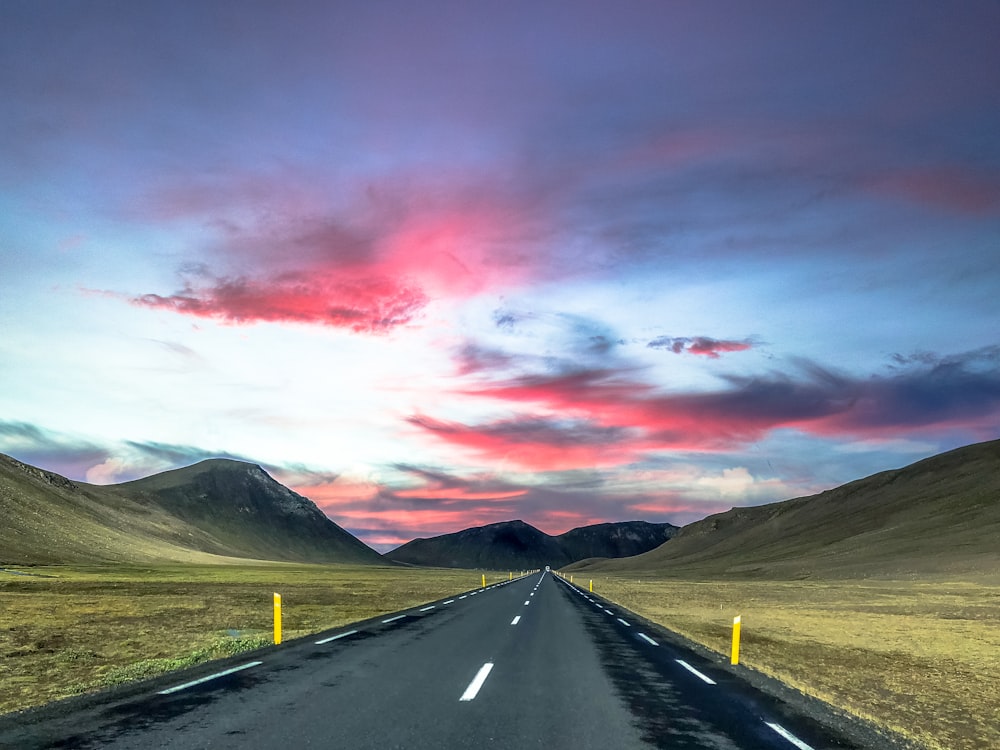 gray concrete road near green grass field and mountain under gray clouds