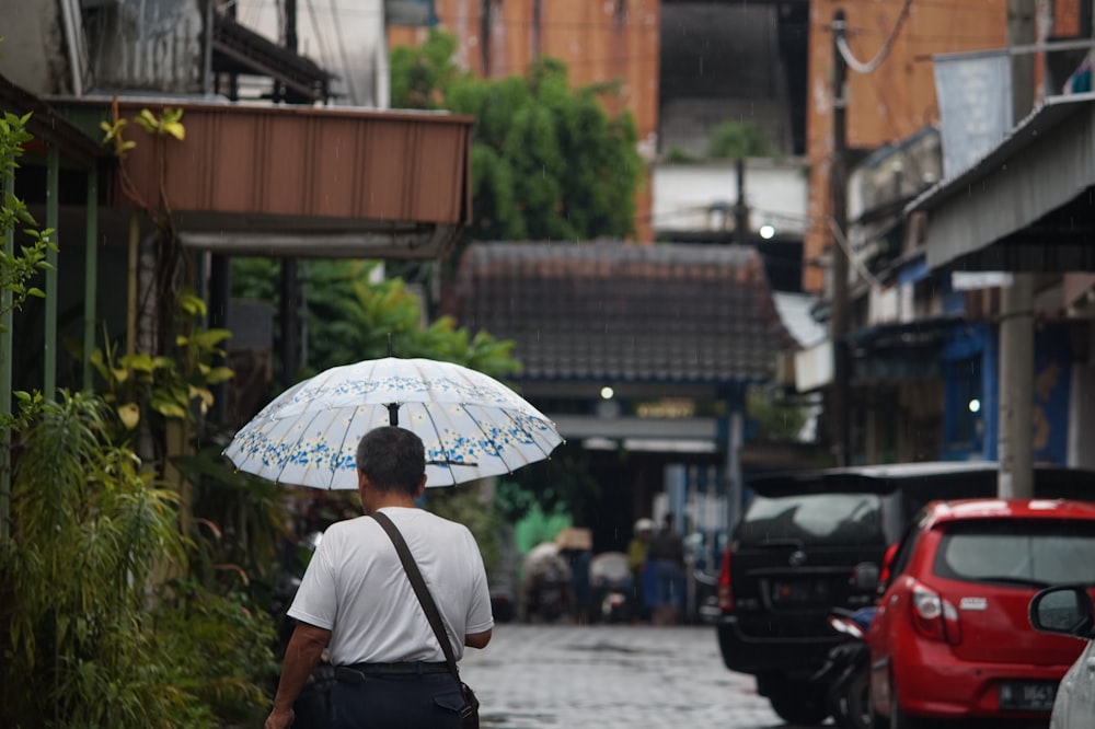 man in black shirt holding umbrella walking on street during daytime