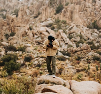 man in black jacket and brown pants standing on brown rock during daytime