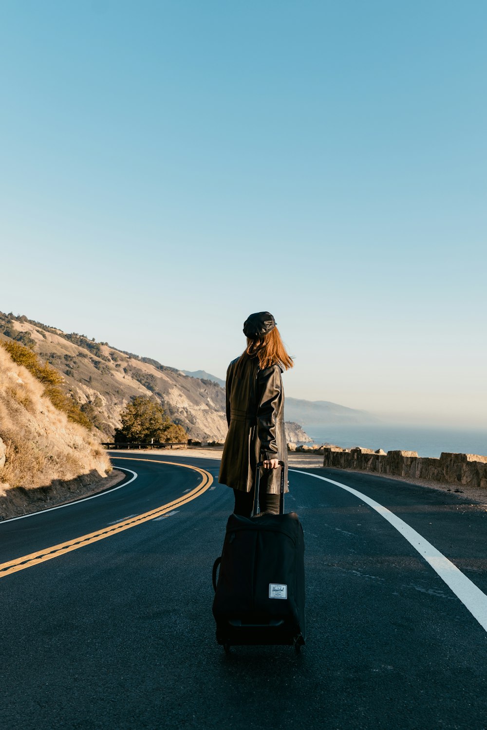 woman in brown jacket standing on the road during daytime