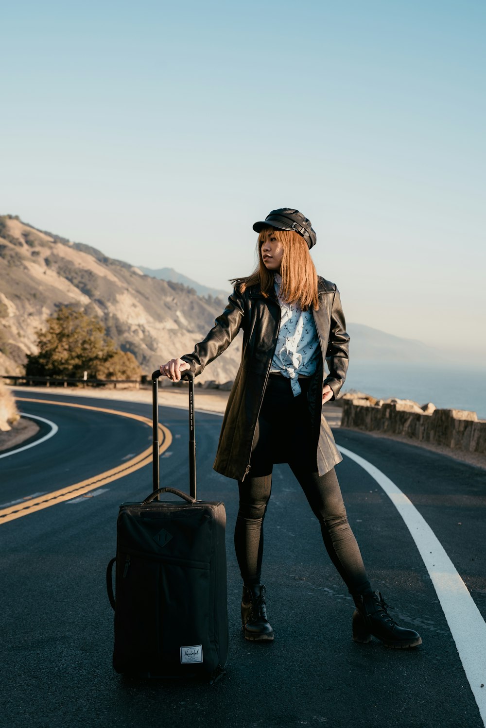 Femme en veste en cuir noir et pantalon noir debout sur la route pendant la journée