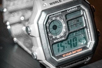 A close-up view of a digital wristwatch with a squared face, displaying time in a large digital format. The watch features multiple functions including a stopwatch and alarm, as indicated by various dials and labels. The watch is marked with the brand name 'CASIO' and a note about a 10-year battery life.